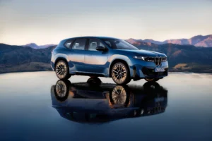 ventas de BMW eléctricos: BMW iX3 azul reflejado sobre agua con montañas.