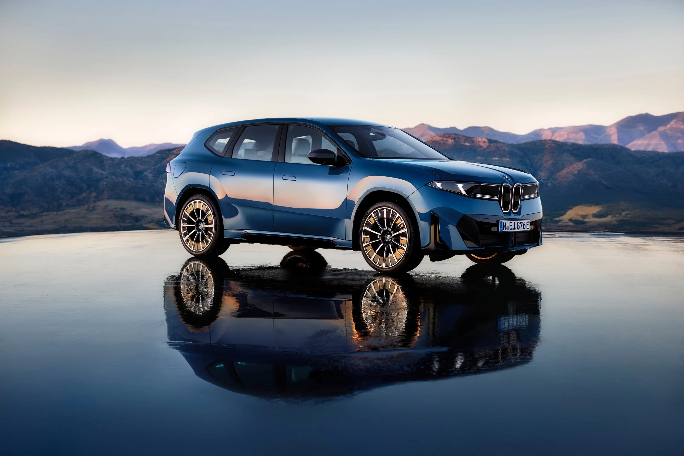 ventas de BMW eléctricos: BMW iX3 azul reflejado sobre agua con montañas.