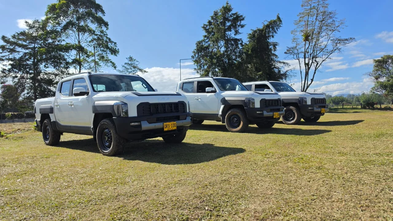 negocio corporativo de Kia: Tres camionetas Kia Tasman blancas en un campo.