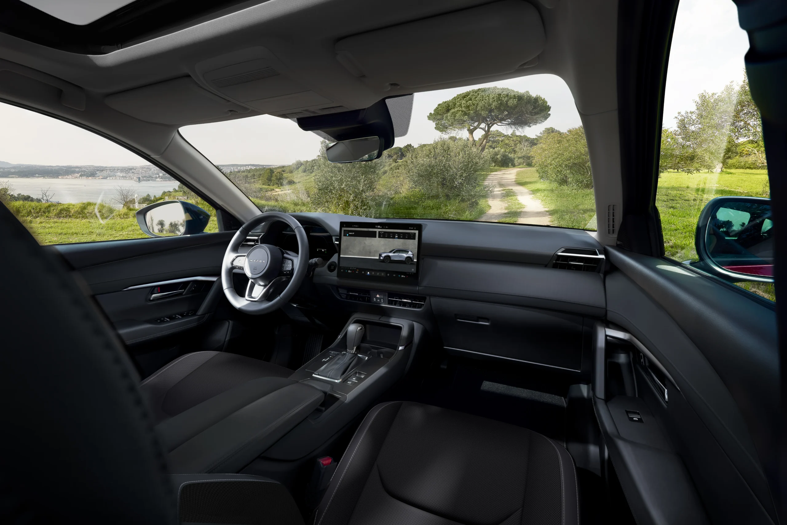 Interior del Mazda CX-5 Híbrida con pantalla central y paisaje exterior.