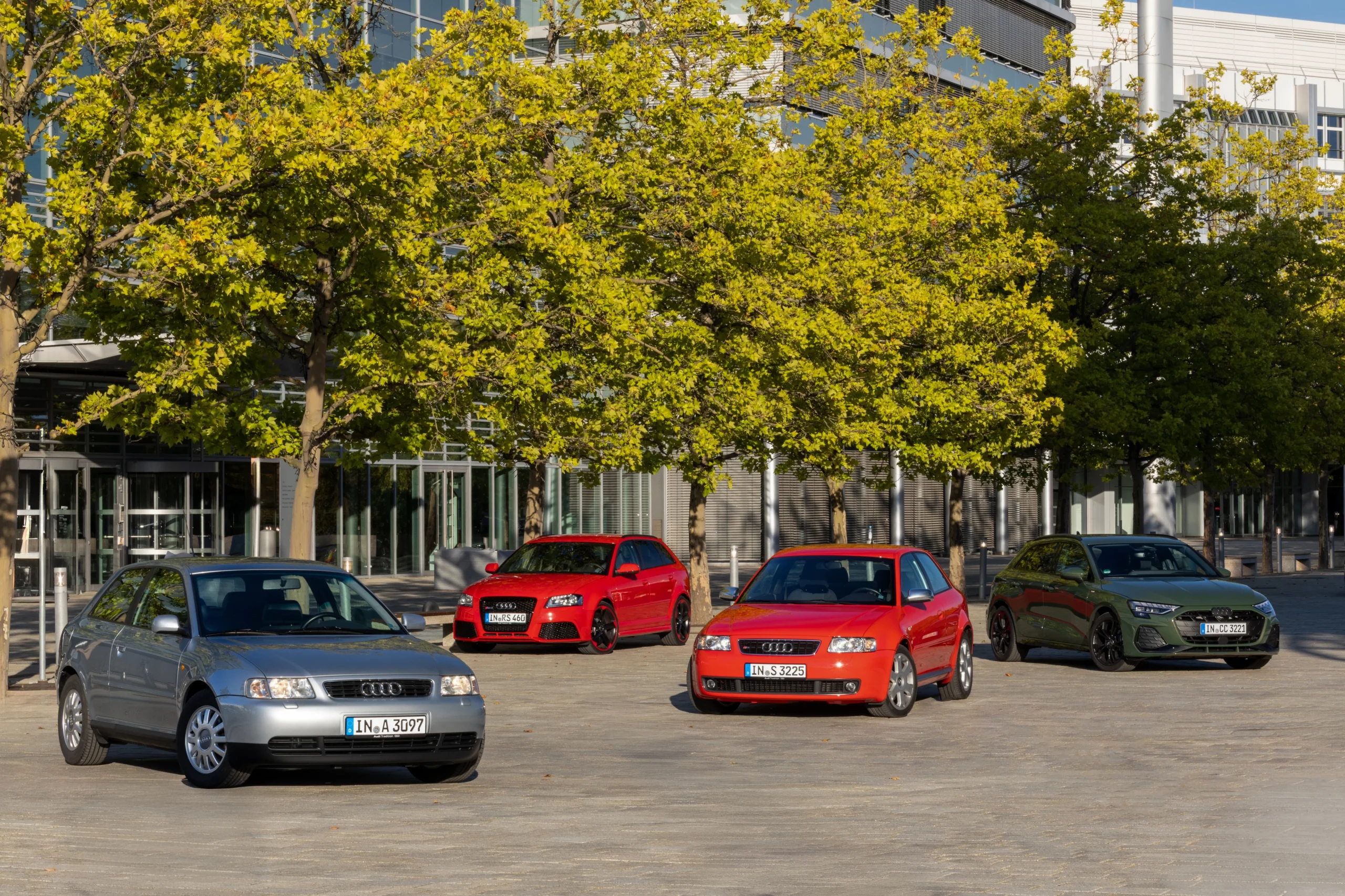 historia de Audi A3: Cuatro Audi A3 de distintas generaciones frente a edificio corporativo.