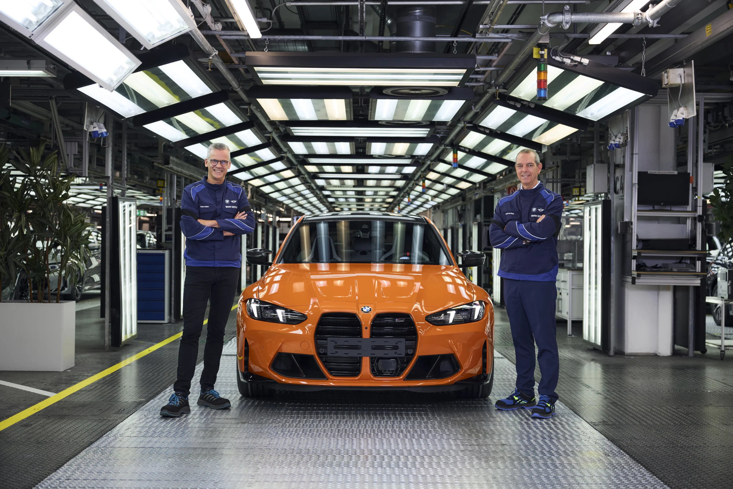 Dos hombres junto a un BMW M3 naranja en fábrica.