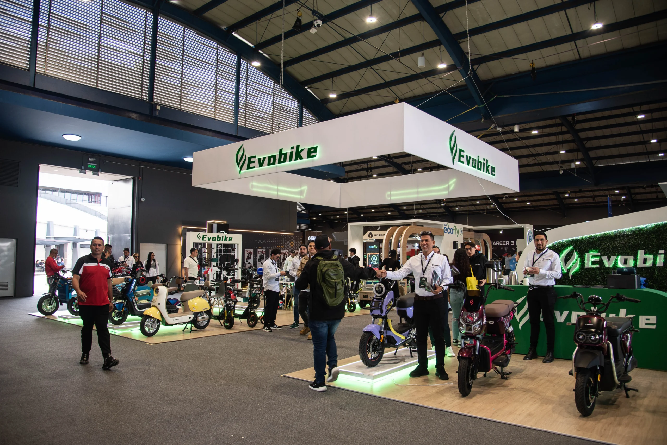 movilidad alternativa Expo2Ruedas: Visitantes en un evento de movilidad eléctrica con scooters y bicicletas.