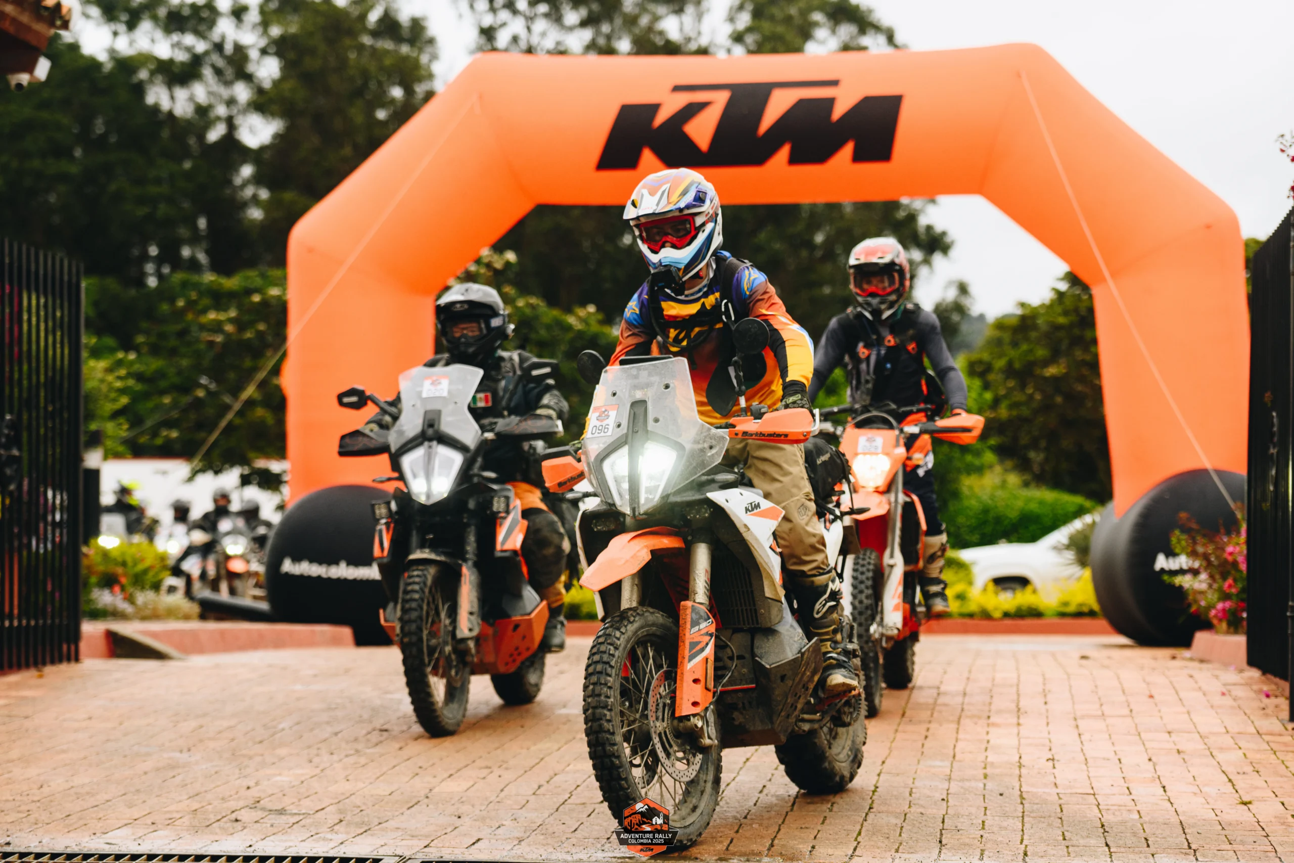 moto de alto cilindraje: Motociclistas KTM ingresando a evento bajo arco inflable naranja.