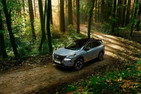 conducción eficiente de Nissan: Nissan X-Trail gris en ruta de bosque ecológico.